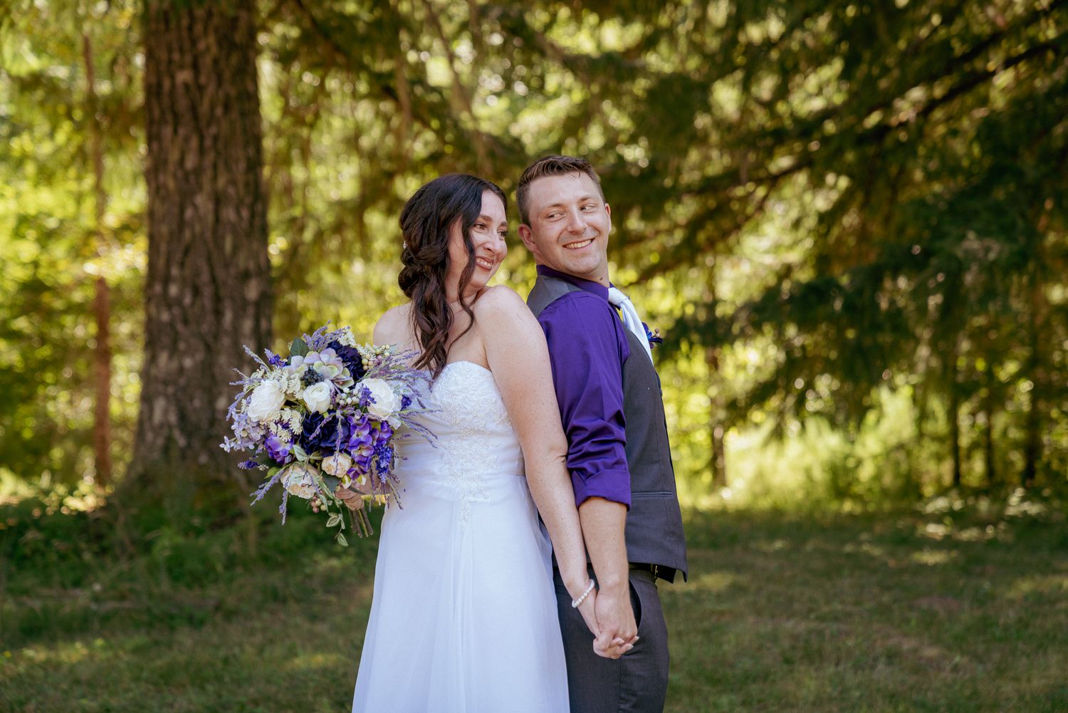 Bride with purple florals smiles at partner, joyful PNW forest wedding.