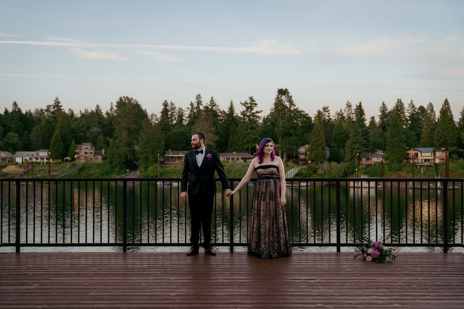 Couple standing on a dock overlooking calm lake. Peaceful wedding portrait with nature view.