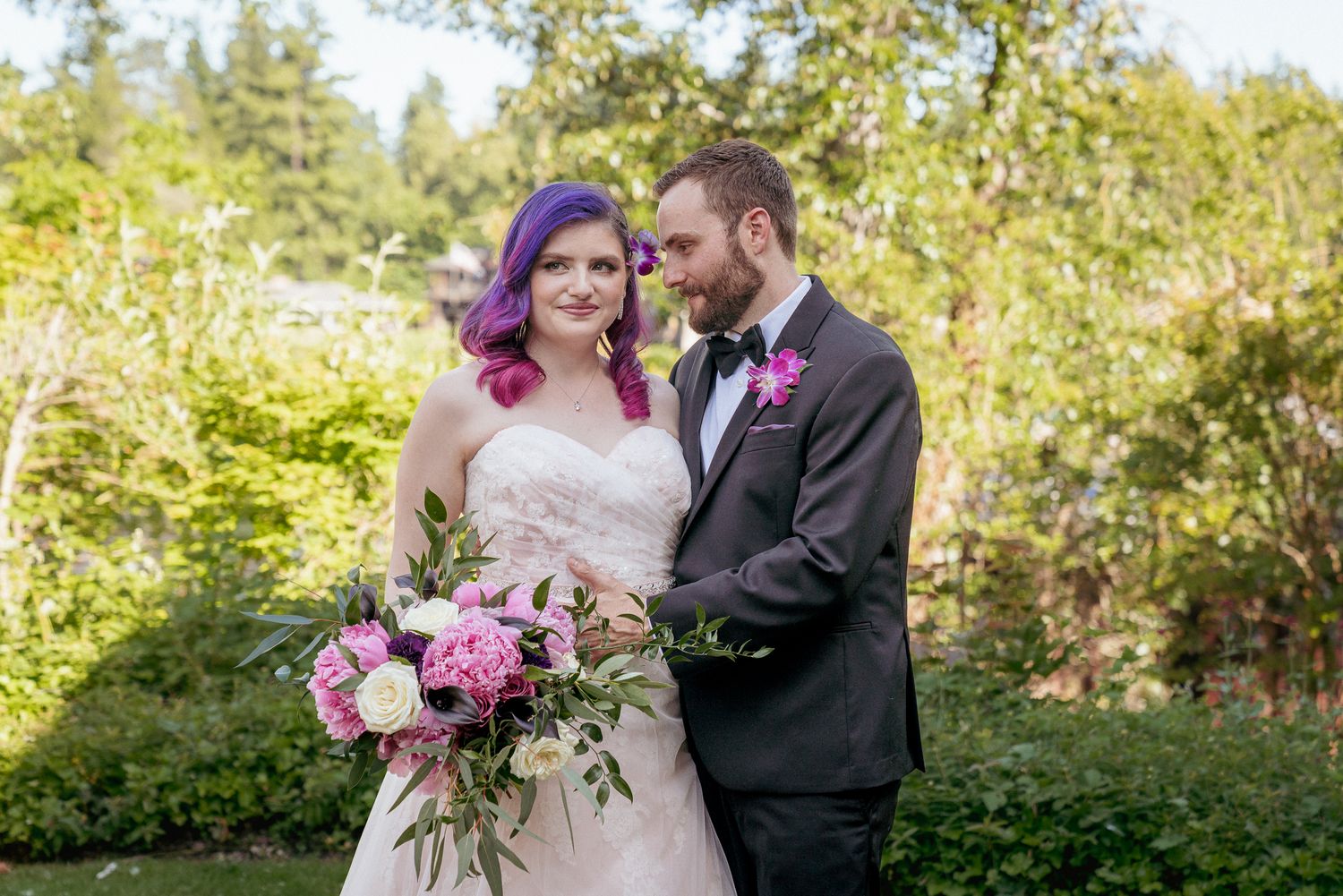 Bride with purple hair and groom holding pink bouquet in garden setting.