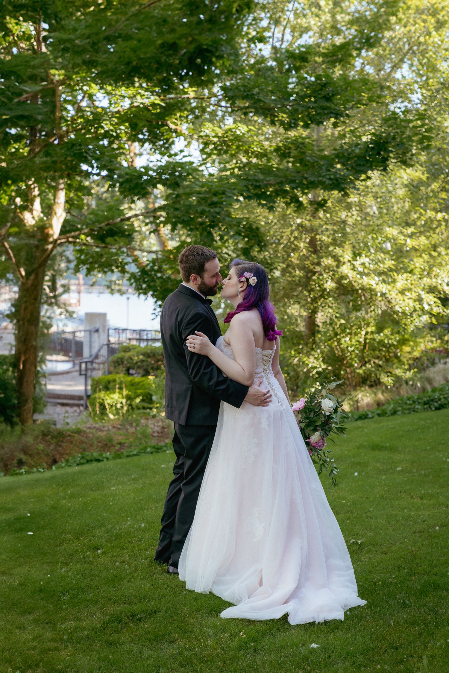 A newlywed couple shares a kiss under lush trees, intimate PNW wedding.