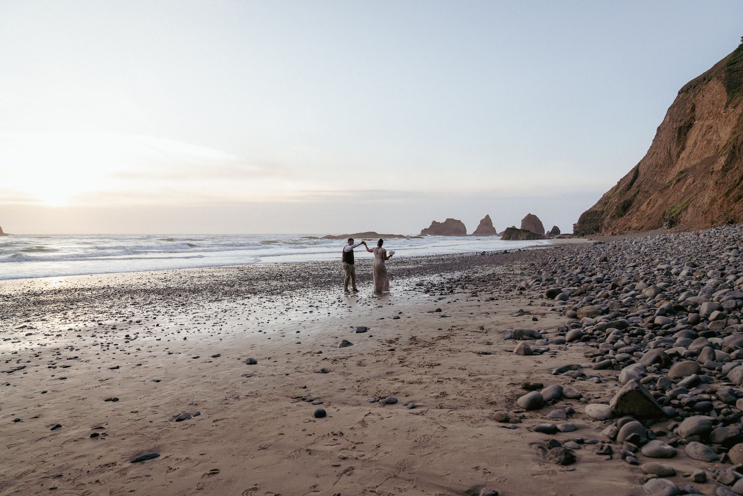 Interracial couple walks barefoot on Oregon Coast at sunset, dreamy PNW beach elopement.