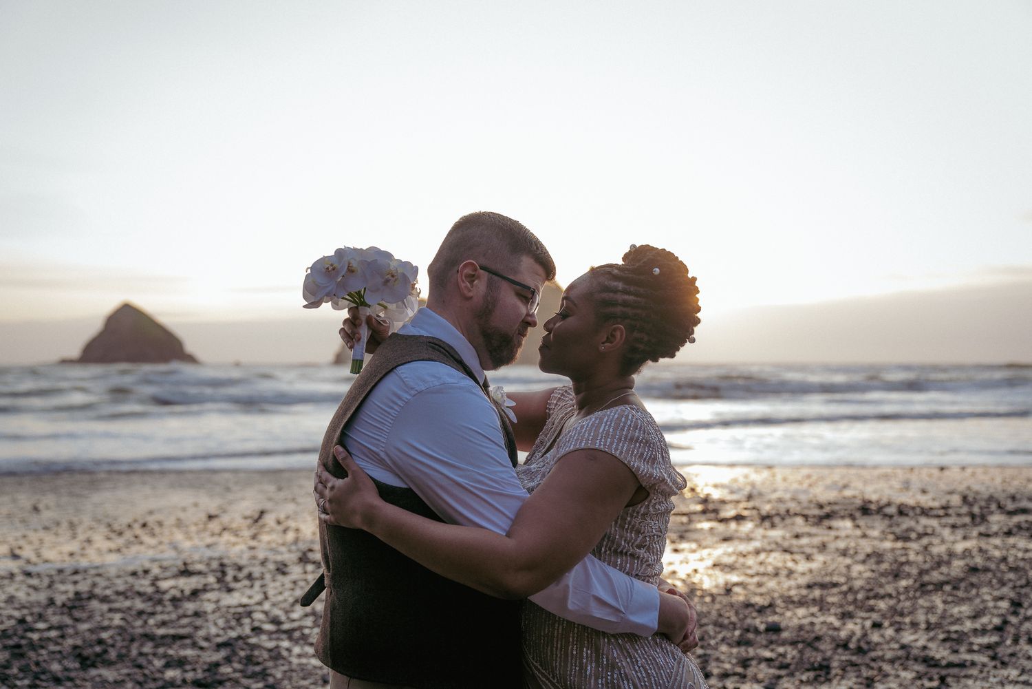 Interracial couple kisses on the beach, golden Oregon Coast sunset.