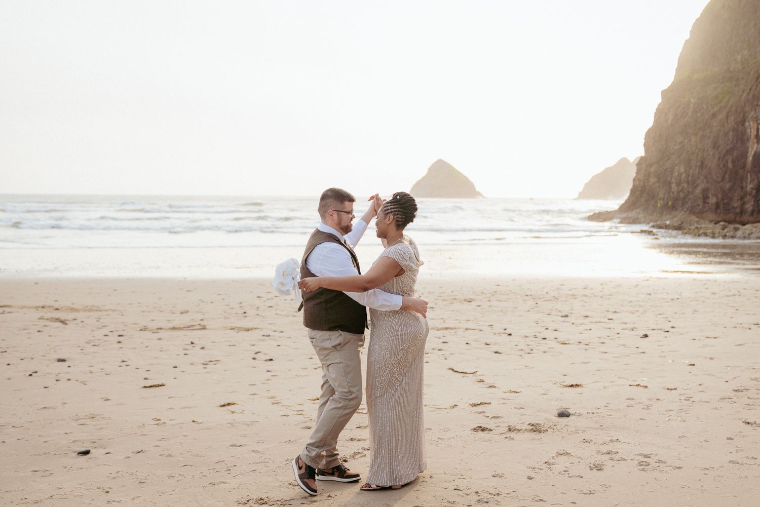 Interracial couple walks barefoot on Oregon Coast beach at sunset.