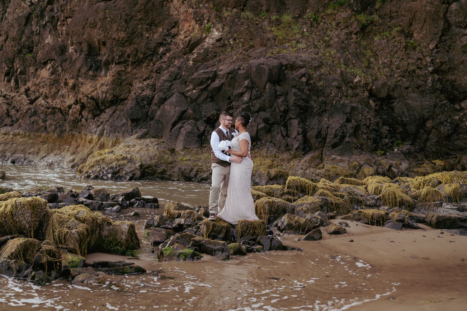 Newlyweds embrace on rocky Oregon Coast, adventurous elopement.