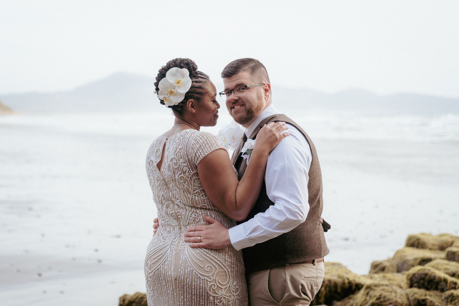 Black bride and white groom embrace on the beach, Oregon love story.