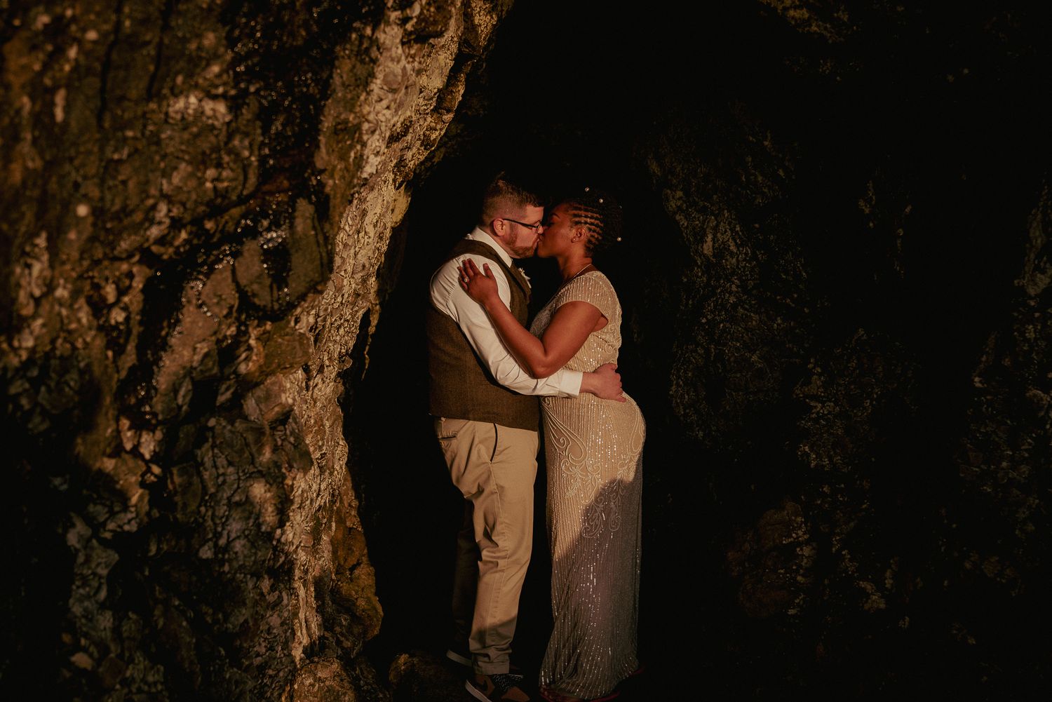 Interracial couple kisses in dark cave, adventurous Oregon elopement.