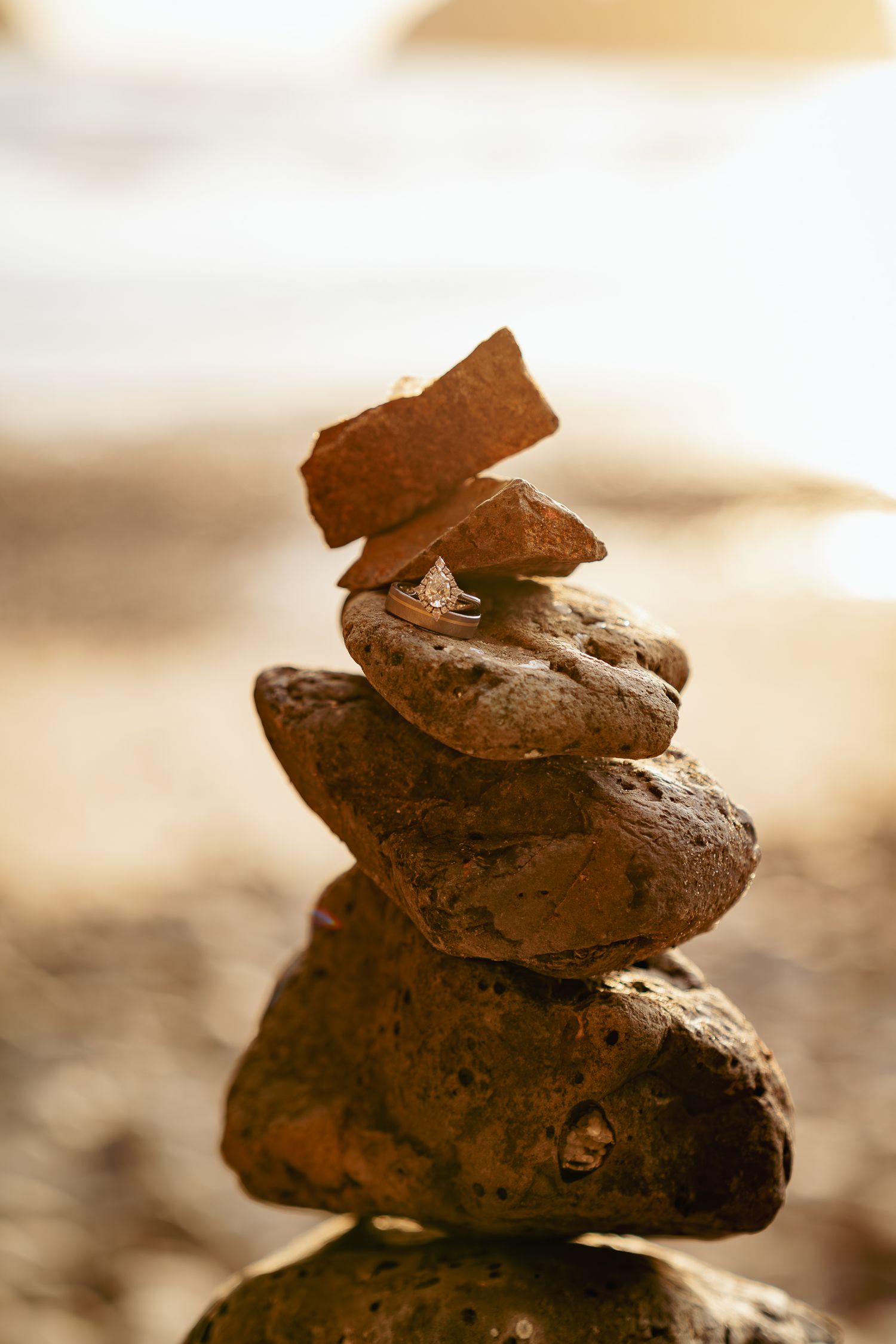 Stack of smooth stones with wedding rings in them at sunset, grounding detail from Oregon Coast.
