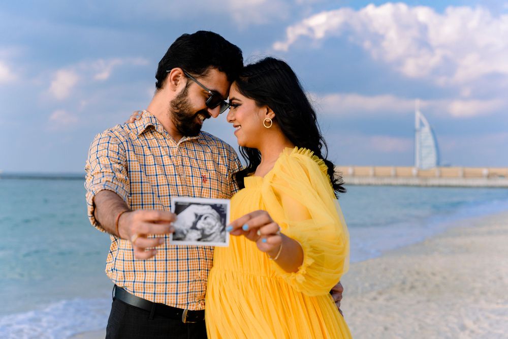 A couple on the beach holding an ultrasound photo with the Burj Al Arab in the background.