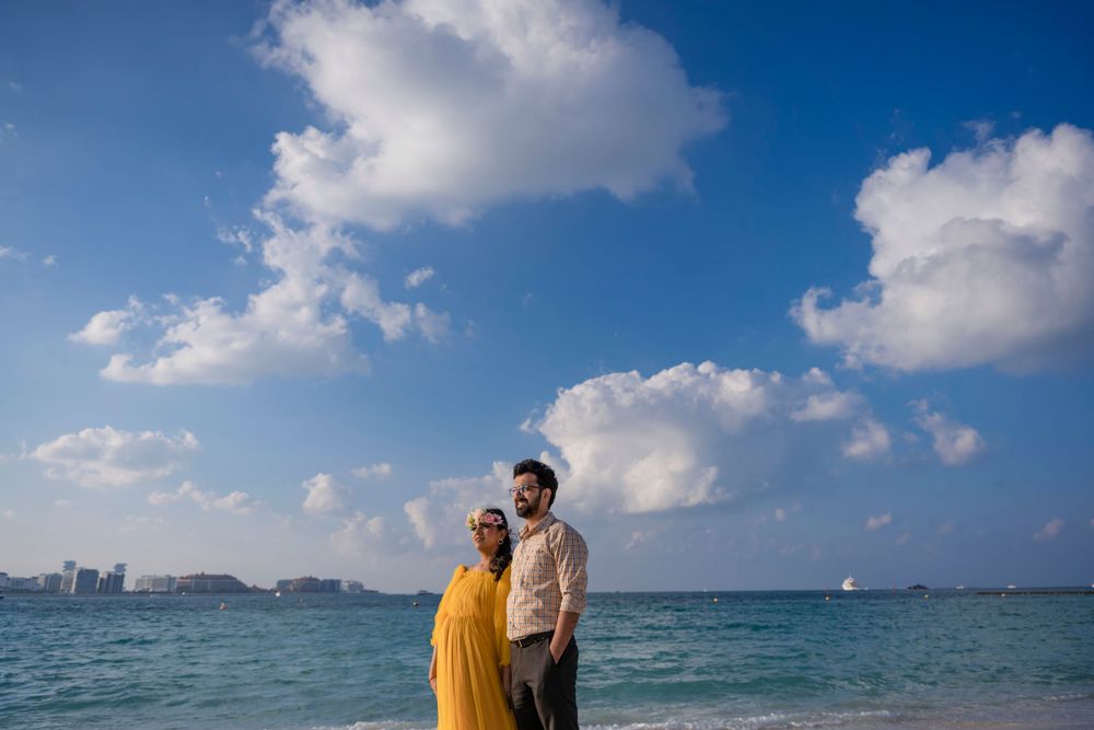 A couple poses on the beach in Dubai with blue waters and white clouds in the background.