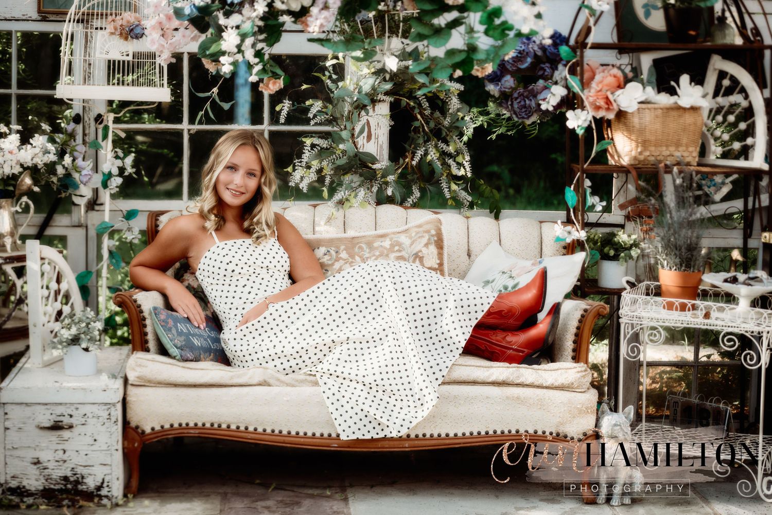 A dreamy garden scene with someone reclining on a vintage sofa surrounded by flowers and greenery.