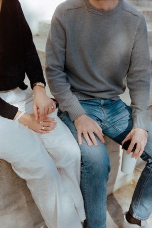 Two people sitting close together on stone steps, showing hands and casual attire.