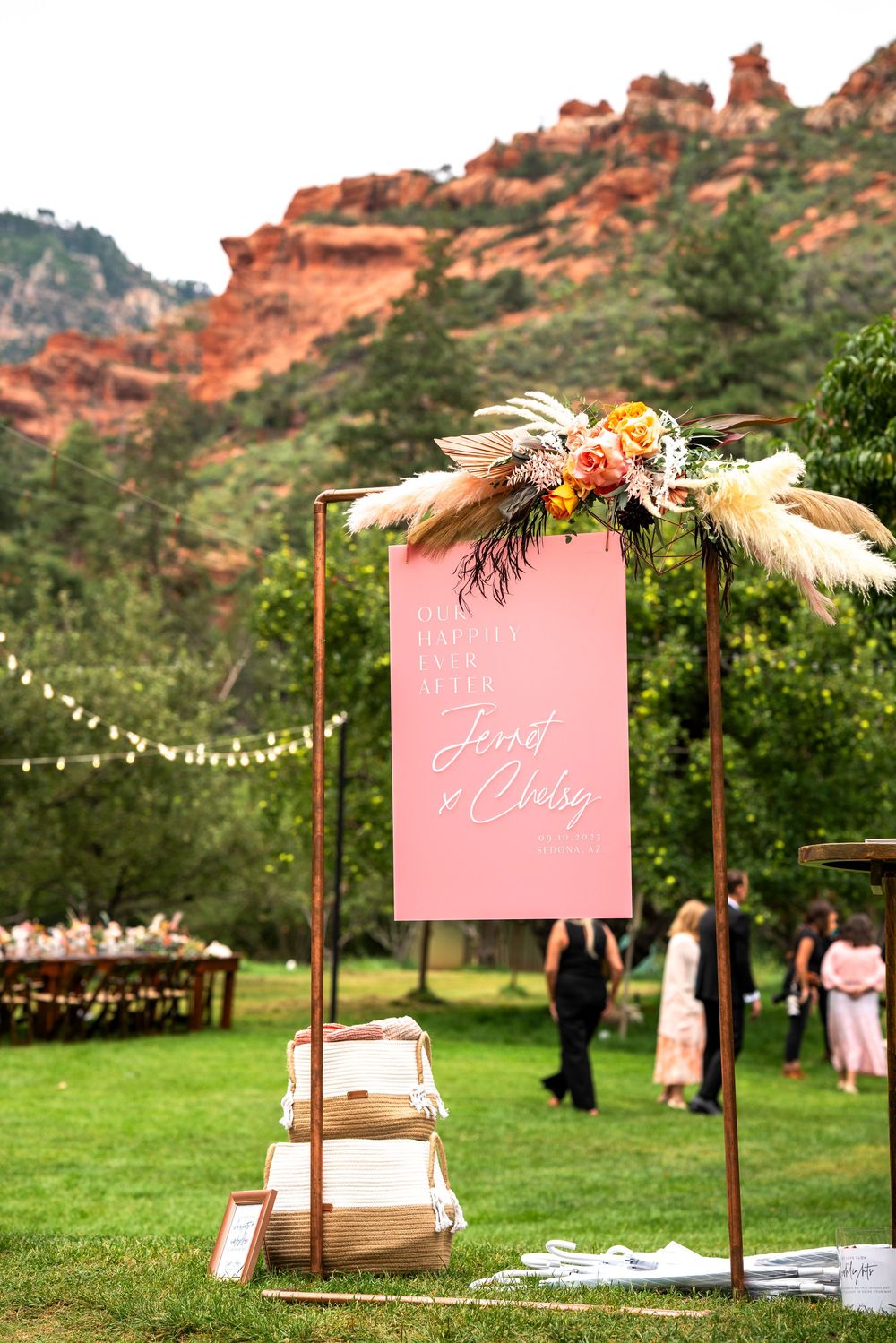 Outdoor wedding sign on copper stand with floral decor, pink banner, red rock mountains backdrop in Colorado.