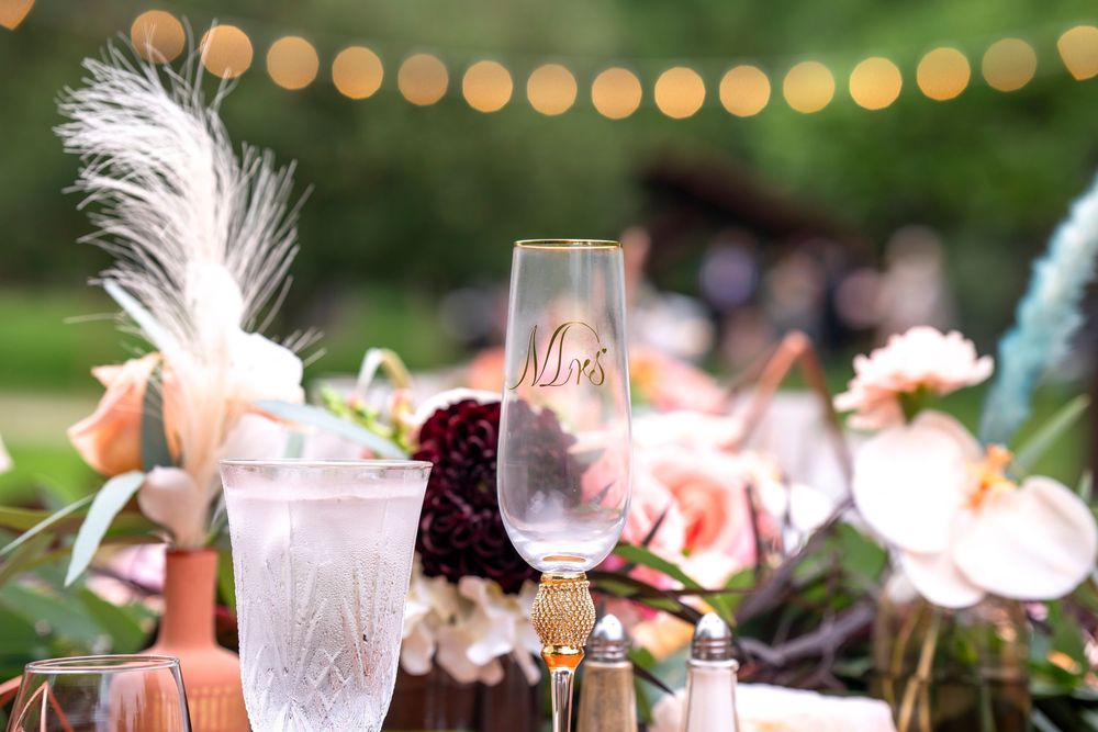 Elegant wedding table setting with Mrs. champagne flute, crystal glassware, pampas grass, and floral arrangements under string lights.