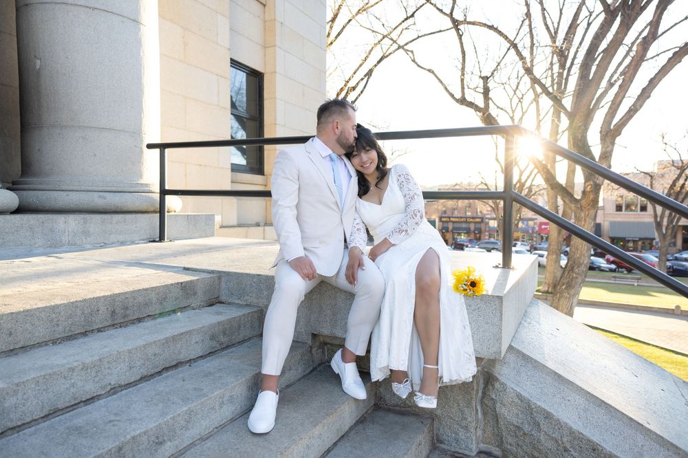 A couple in matching white outfits sits together on stone steps at sunset with daffodils nearby.