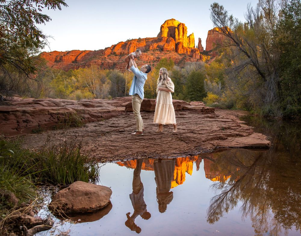 Couple standing on red rocks in Sedona Arizona with Cathedral Rock reflection in water at golden hour sunset.