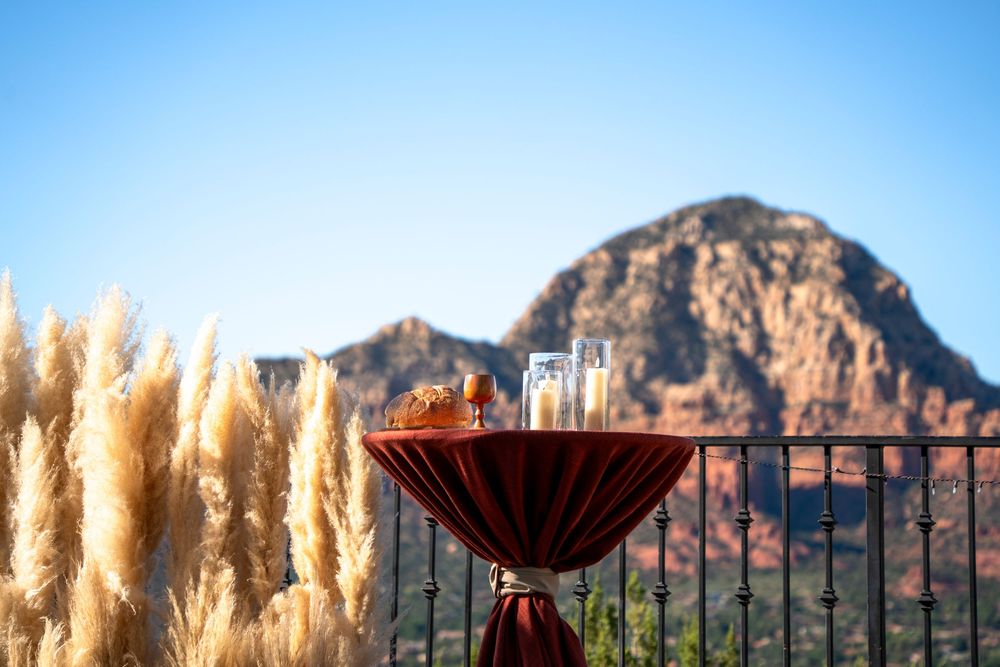 Elegant cocktail table with red draping set against Sedona red rock mountains and pampas grass under blue sky.