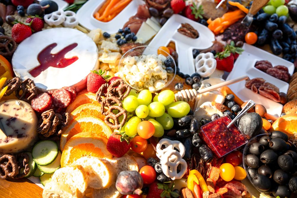 Colorful charcuterie board with grapes, strawberries, oranges, pretzels, cheese, and chocolate arranged decoratively.