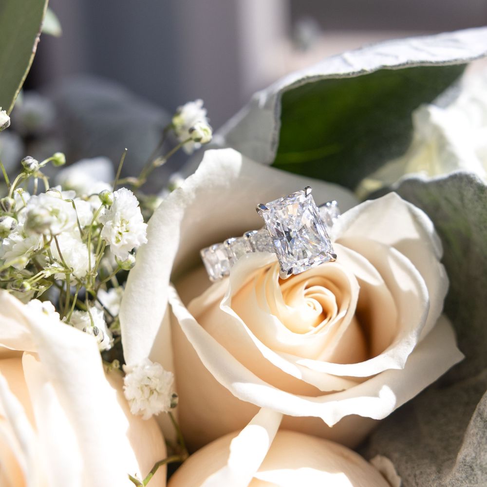 A sparkling diamond engagement ring rests atop delicate peach roses with baby's breath flowers.