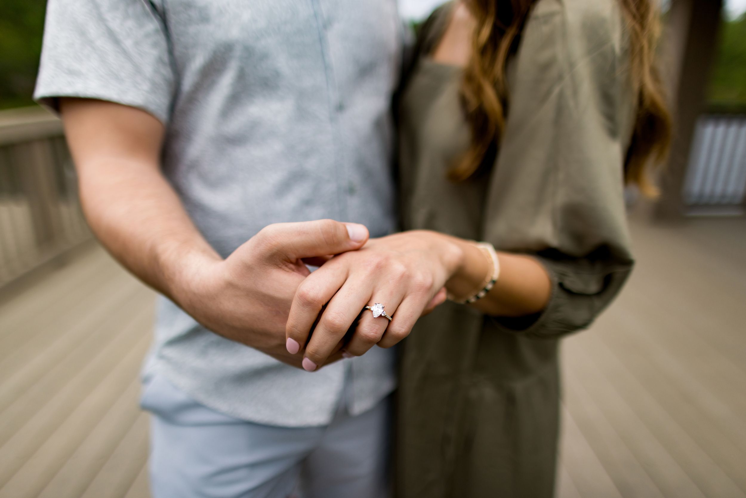 Close-up of hands showing off an engagement ring on wooden deck.