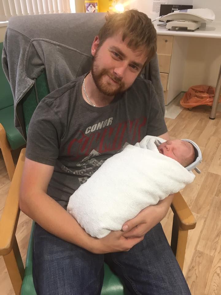 A newborn baby swaddled in white blanket being held in a green chair.