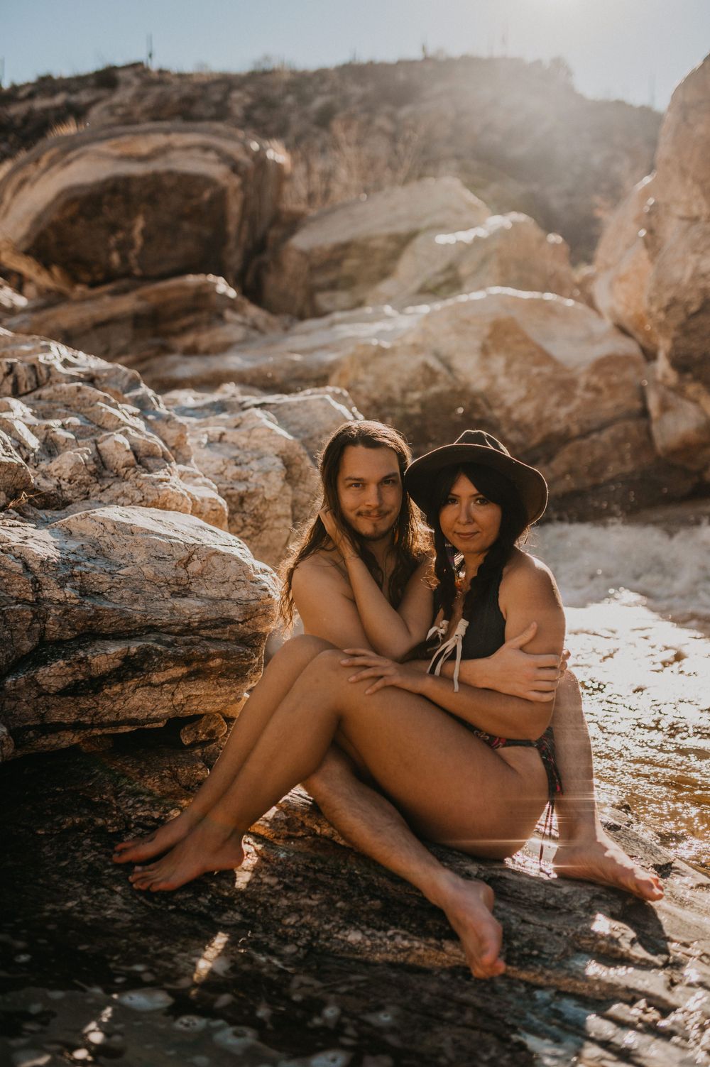 Intimate beach photoshoot on rocky coastal terrain at sunset.