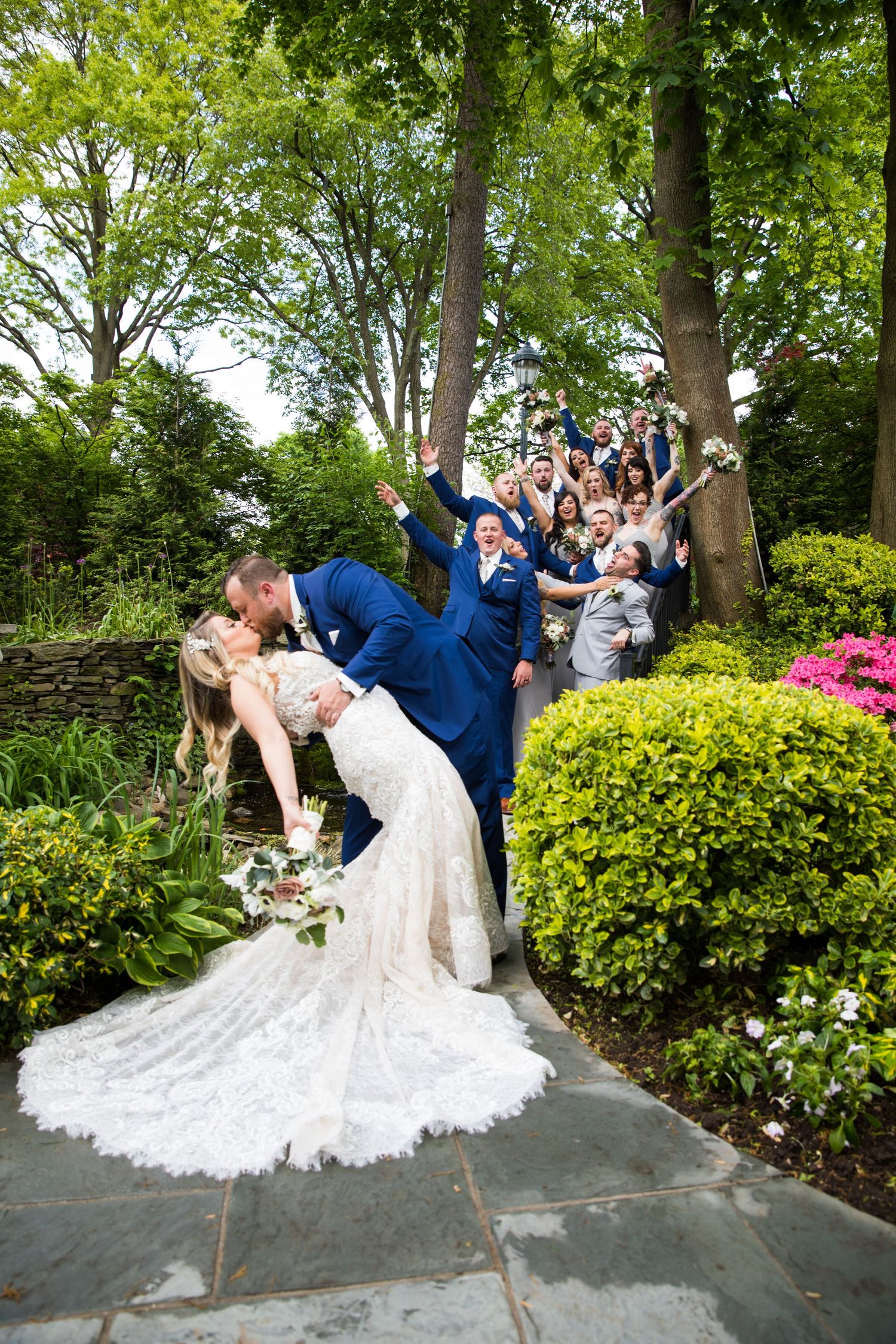 Dramatic wedding dip kiss with cheering guests on garden stairway.