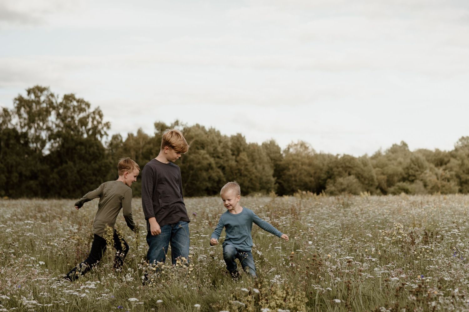 Tre pojkar springer och leker på blomsteräng.