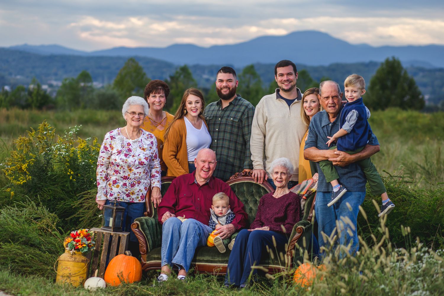 Multi-generational family portrait outdoors with fall pumpkins and mountain backdrop.