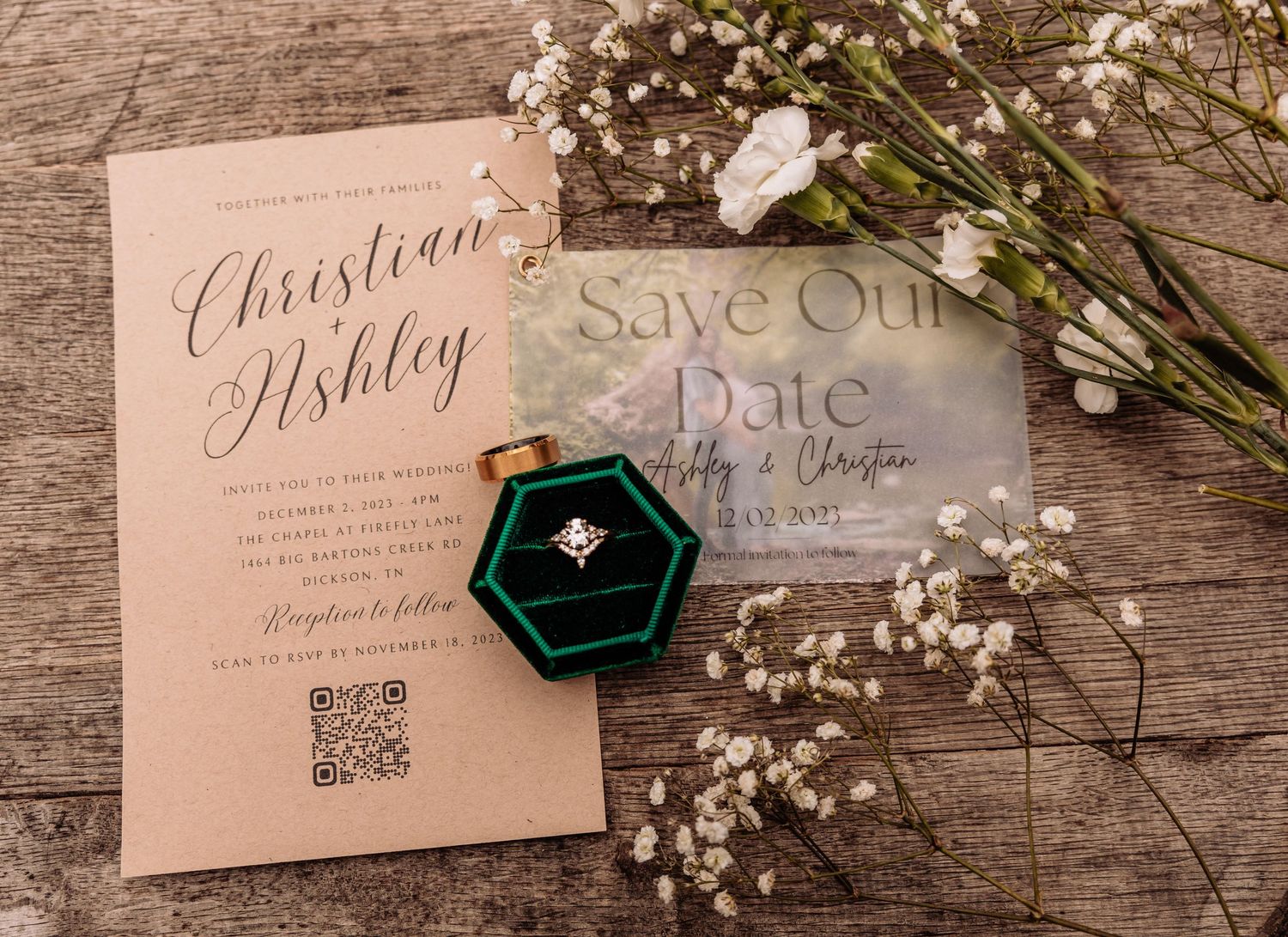 Wedding invitations and save-the-date cards arranged with baby's breath flowers and a green ring box.