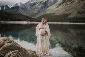 Maternity photo shoot at a mountain lake with dramatic mountain peaks and reflective water.