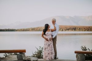 Couple embracing on lakeside deck with mountain landscape in background.