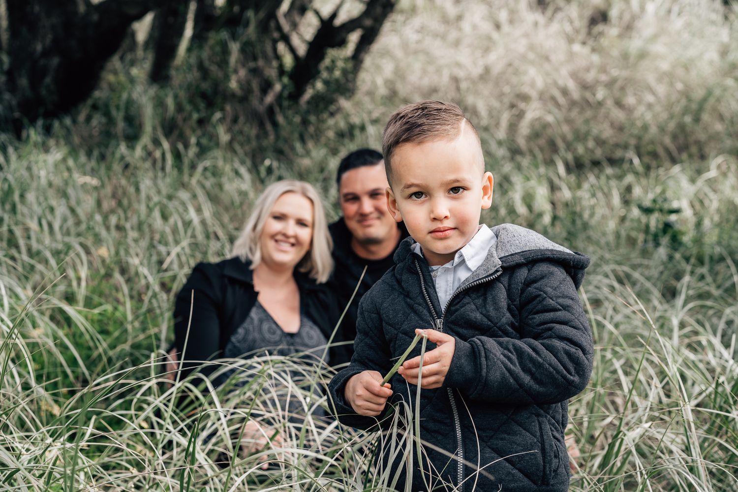 A handsome boy looks for the dinosaur in the camera lens whilst his mum and dad watch.