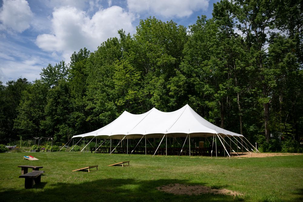 Large white wedding tent set up in a scenic green field surrounded by trees.