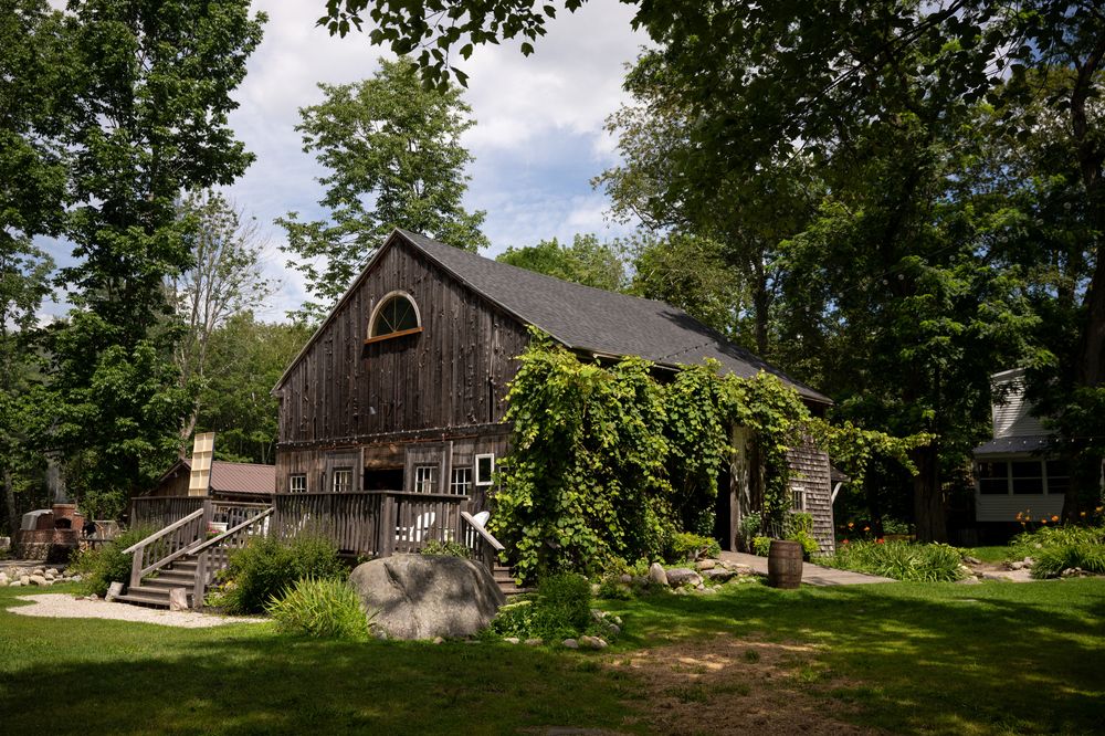 Rustic barn buildings and structures nestled among trees on a rural property.