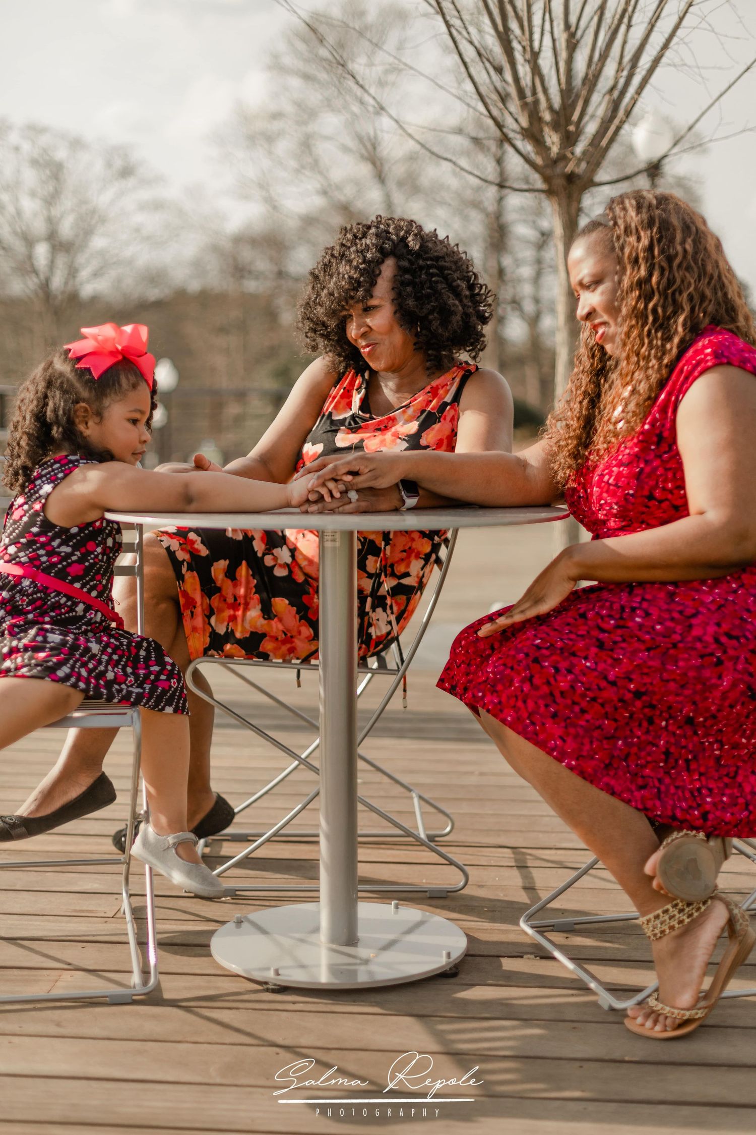 People in red floral dresses sit and interact playfully on outdoor benches.