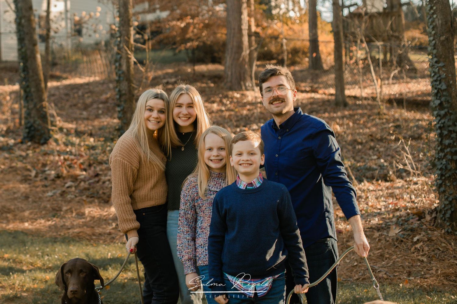 Family members gather for outdoor portraits with autumn trees in background.