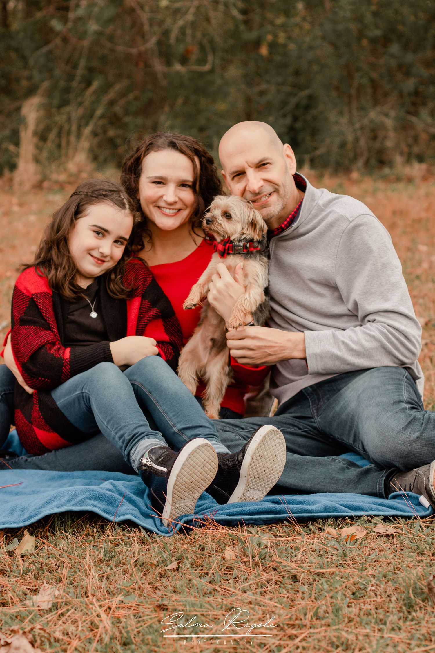 Family lying on blanket with dog during casual outdoor photo shoot.