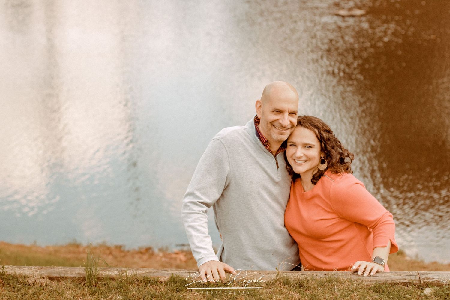 Couple sitting together by a lake during an autumn outdoor photo session.
