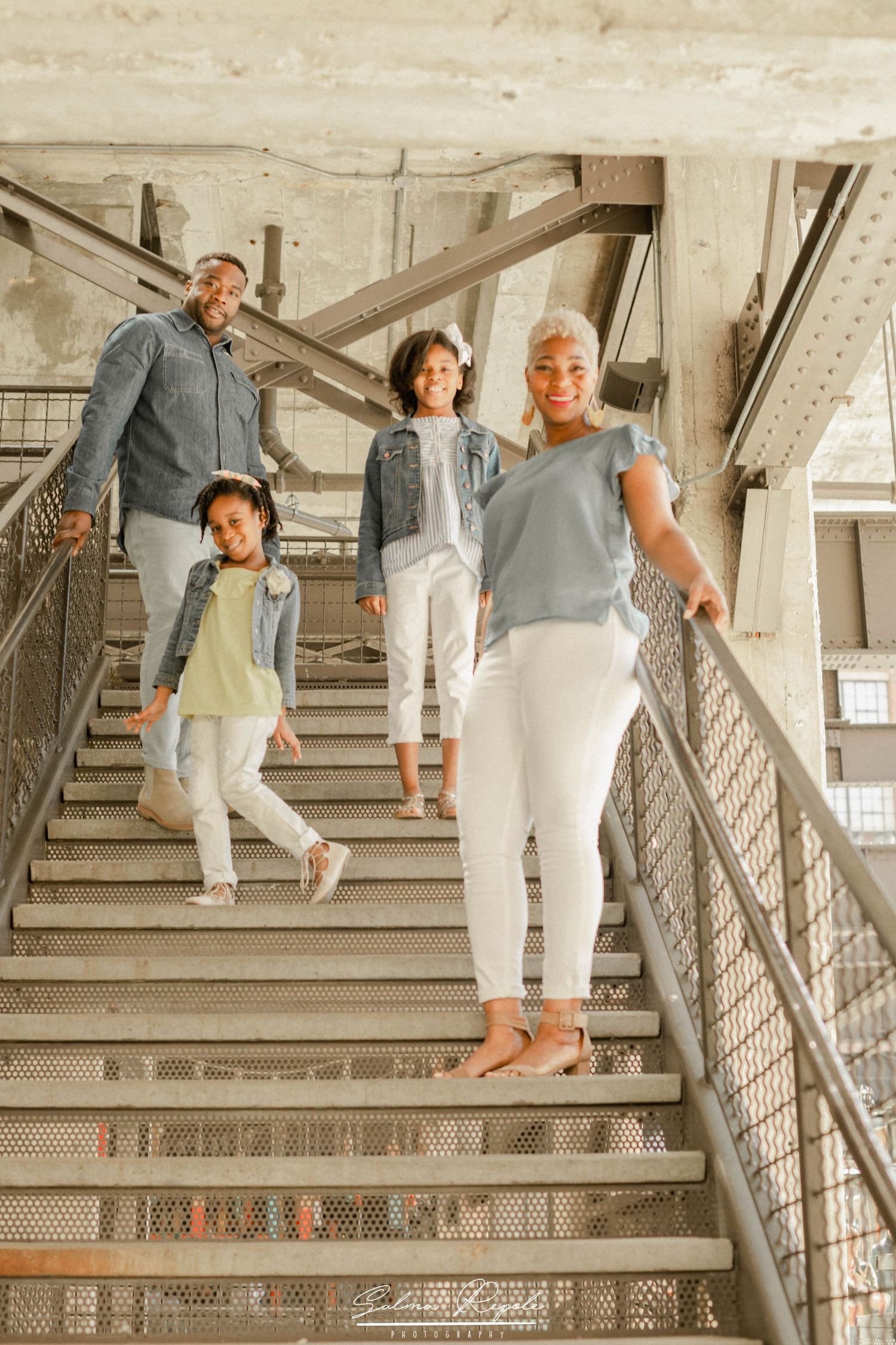 Family in coordinated outfits posing playfully on industrial metal stairs.