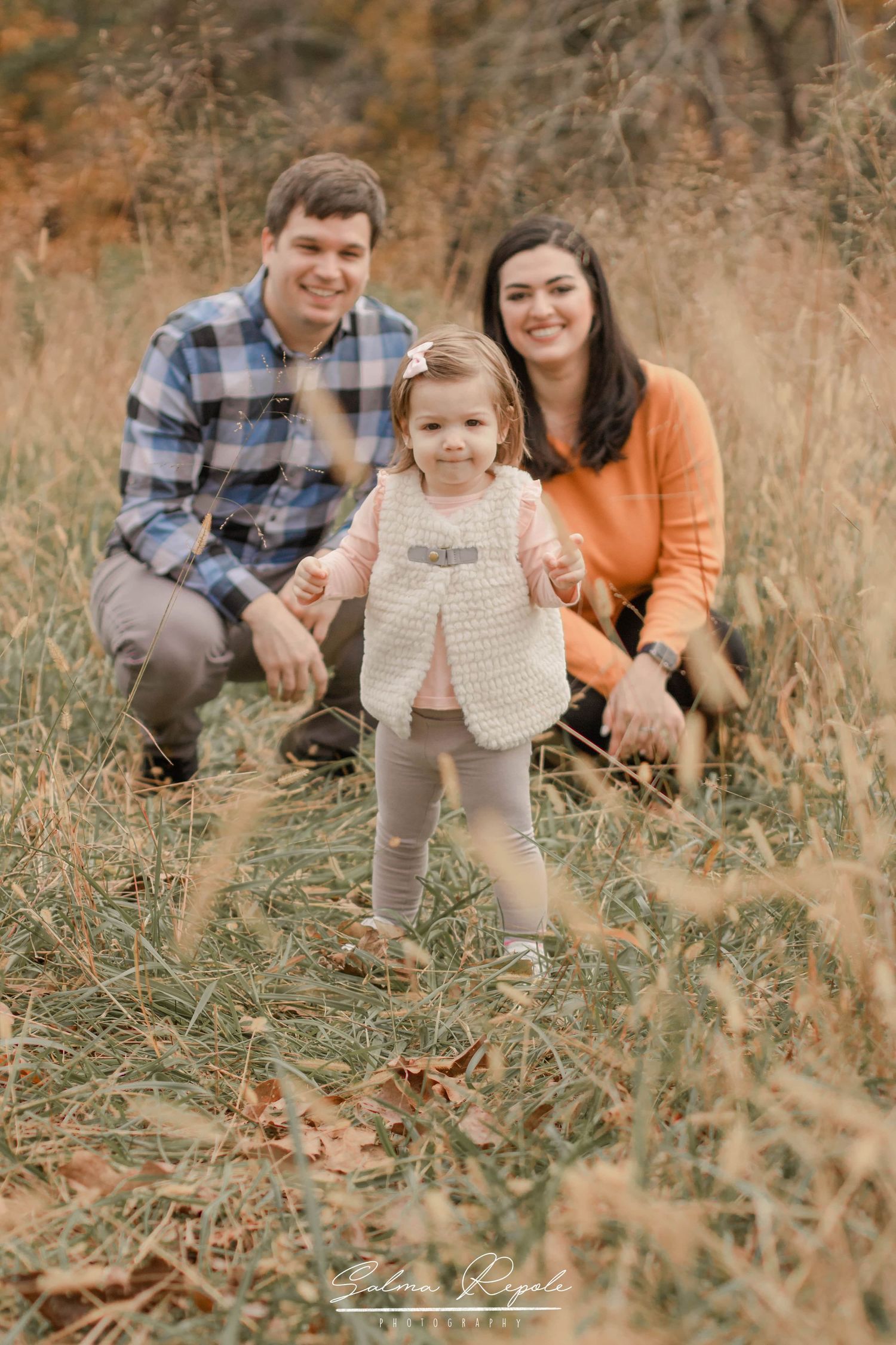 A family plays together in tall autumn grass during a golden hour photoshoot.