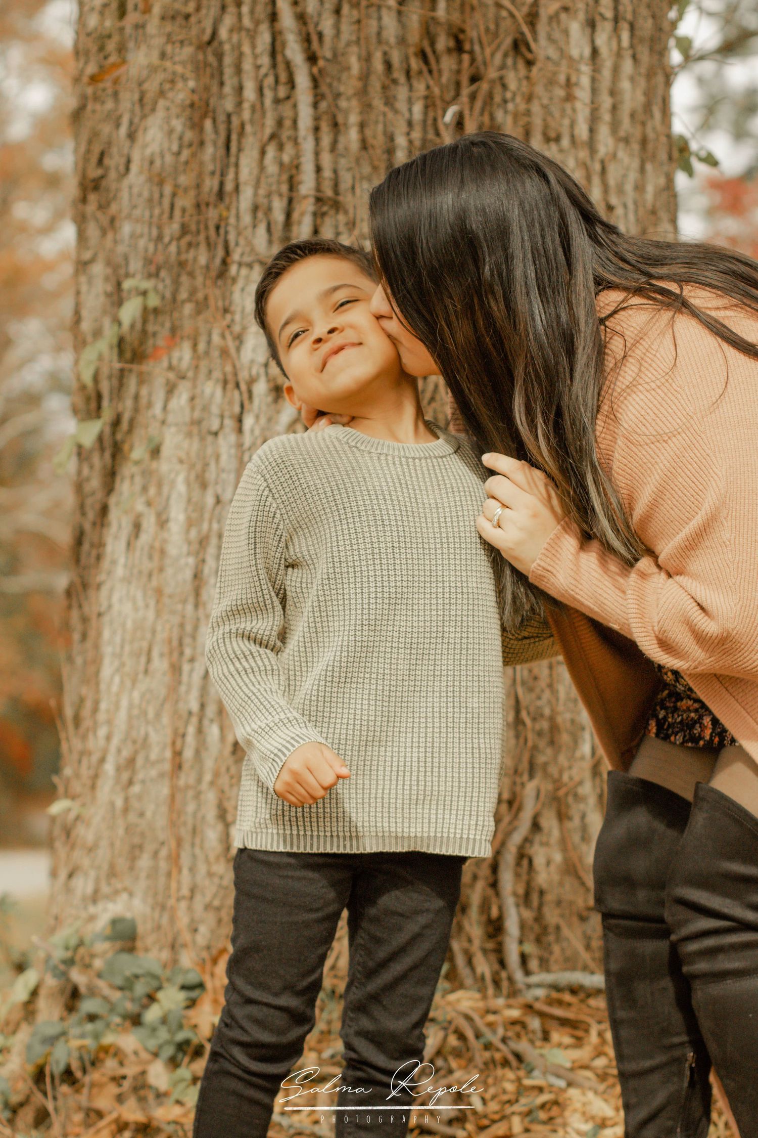 Sweet candid moments captured against a large tree trunk in warm autumn lighting.