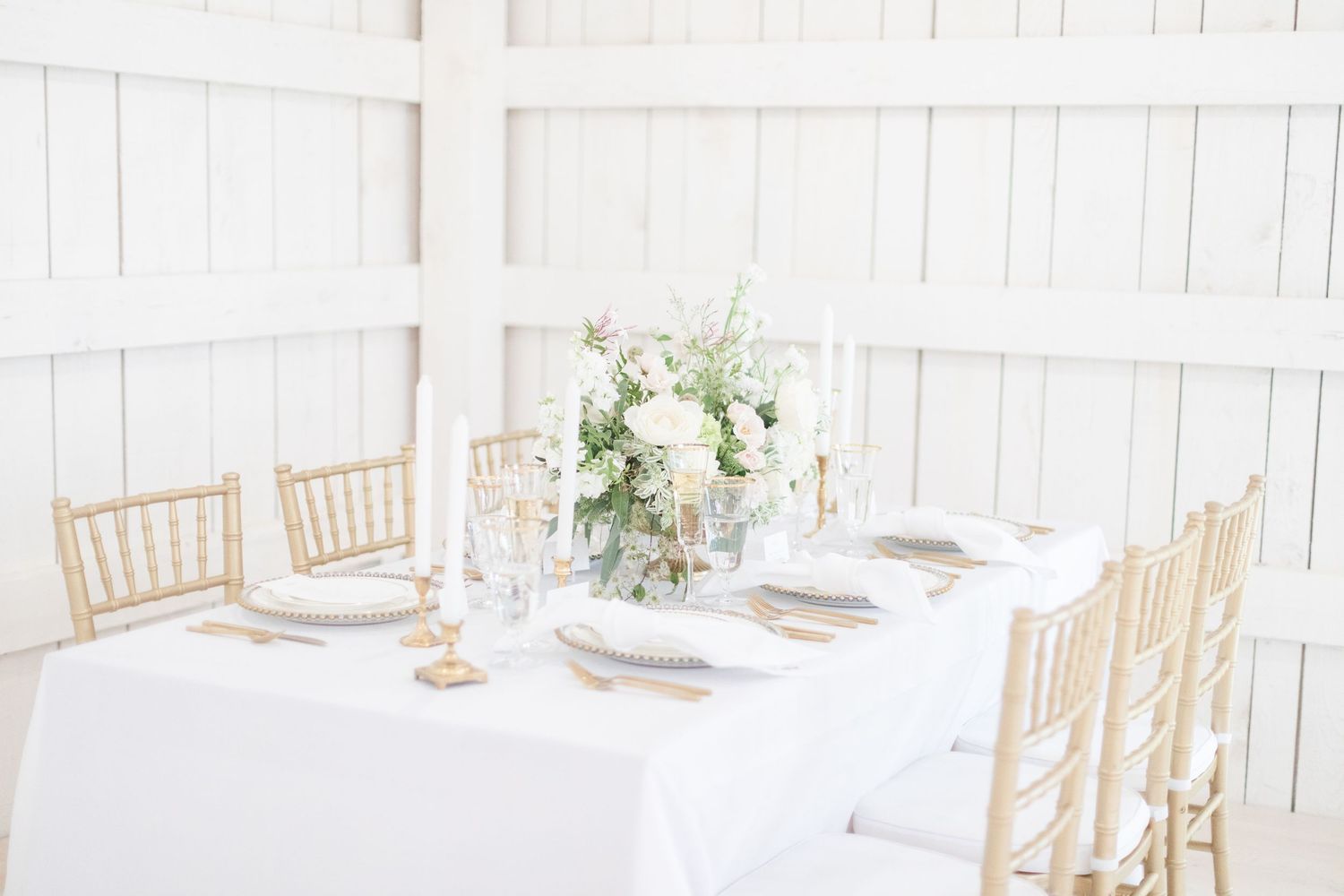 Light and airy indoor wedding reception space with white walls and wooden chiavari chairs.