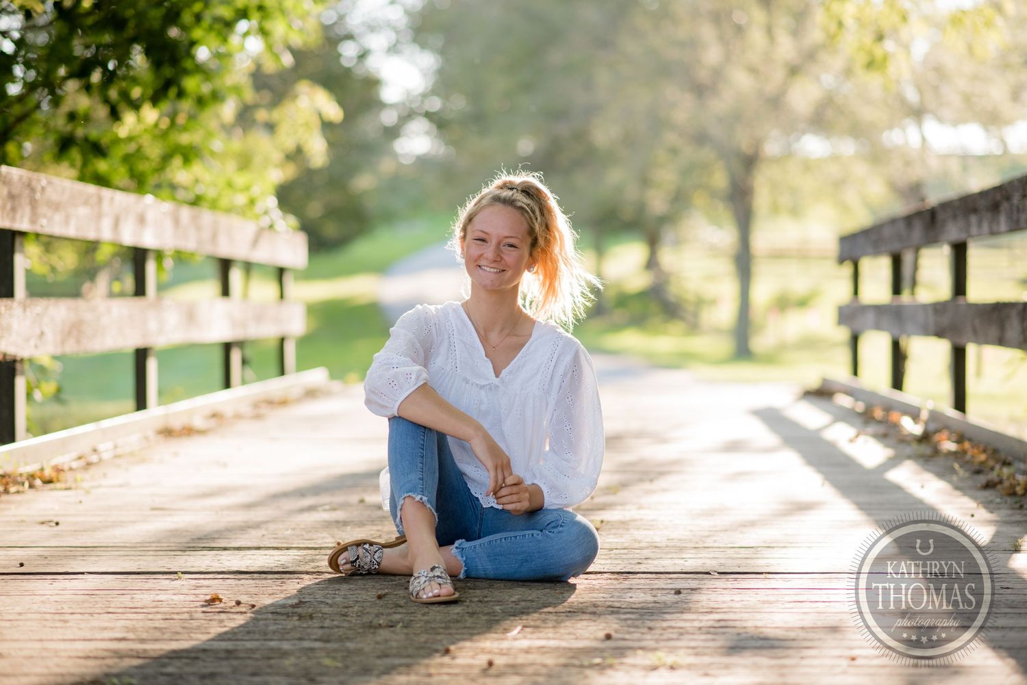 Casual portrait sitting on wooden bridge pathway in morning light.
