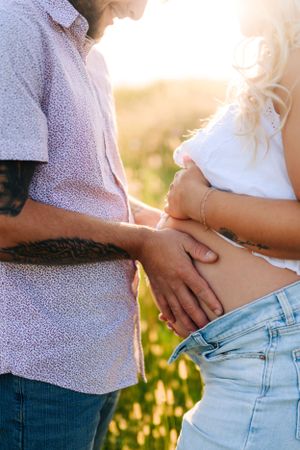 Close-up shot of a couple holding hands over a pregnant belly in golden sunlight.