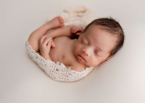 Sleeping newborn wrapped in delicate lace posed on white background.