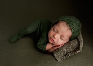 Sleeping newborn wearing green knit outfit resting on textured backdrop.