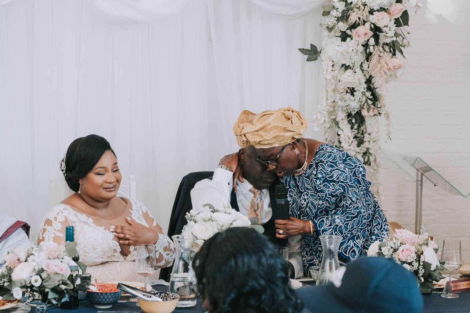 Wedding guests share a joyful moment during a reception celebration at an elegant white-decorated venue.
