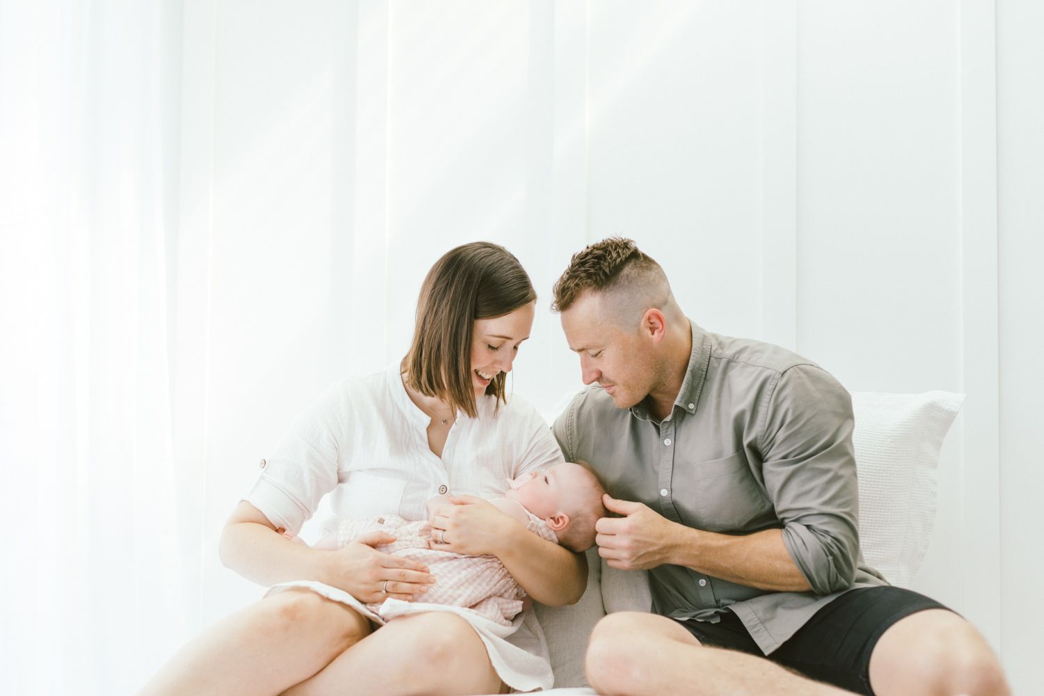 Tender family moment captured with baby on white bed during lifestyle photo session.