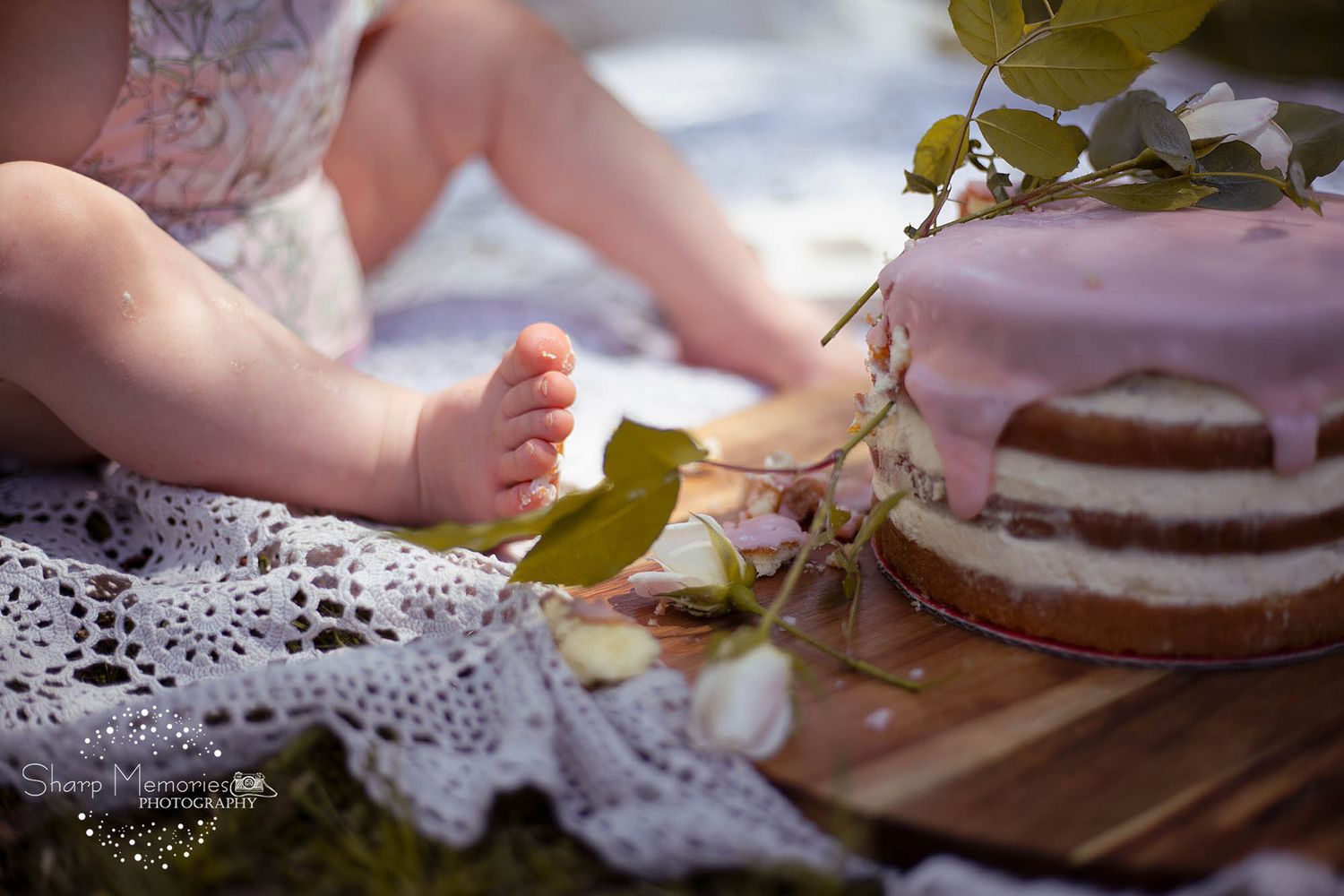 Close-up of bare feet near rustic cake on lace doily outdoors.