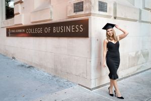 Graduate in black dress and cap poses outside College of Business building.